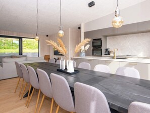 A modern kitchen with a central island, built-in oven, and a dining area with a long table and chairs. - 5 Star Holiday Home in Ebeltoft (Ebeltoft)