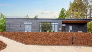 Een modern, tweelaags gebouw met een donkere gevel, grote ramen en een houten dakoverhang.