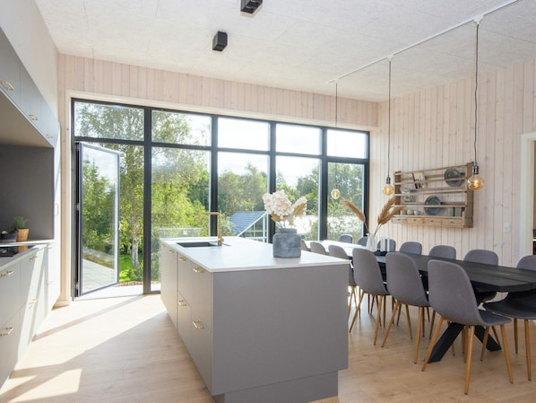 A modern kitchen with a large island, dining area with chairs, and a view through large windows. - 5 Star Holiday Home in Ebeltoft (Ebeltoft)