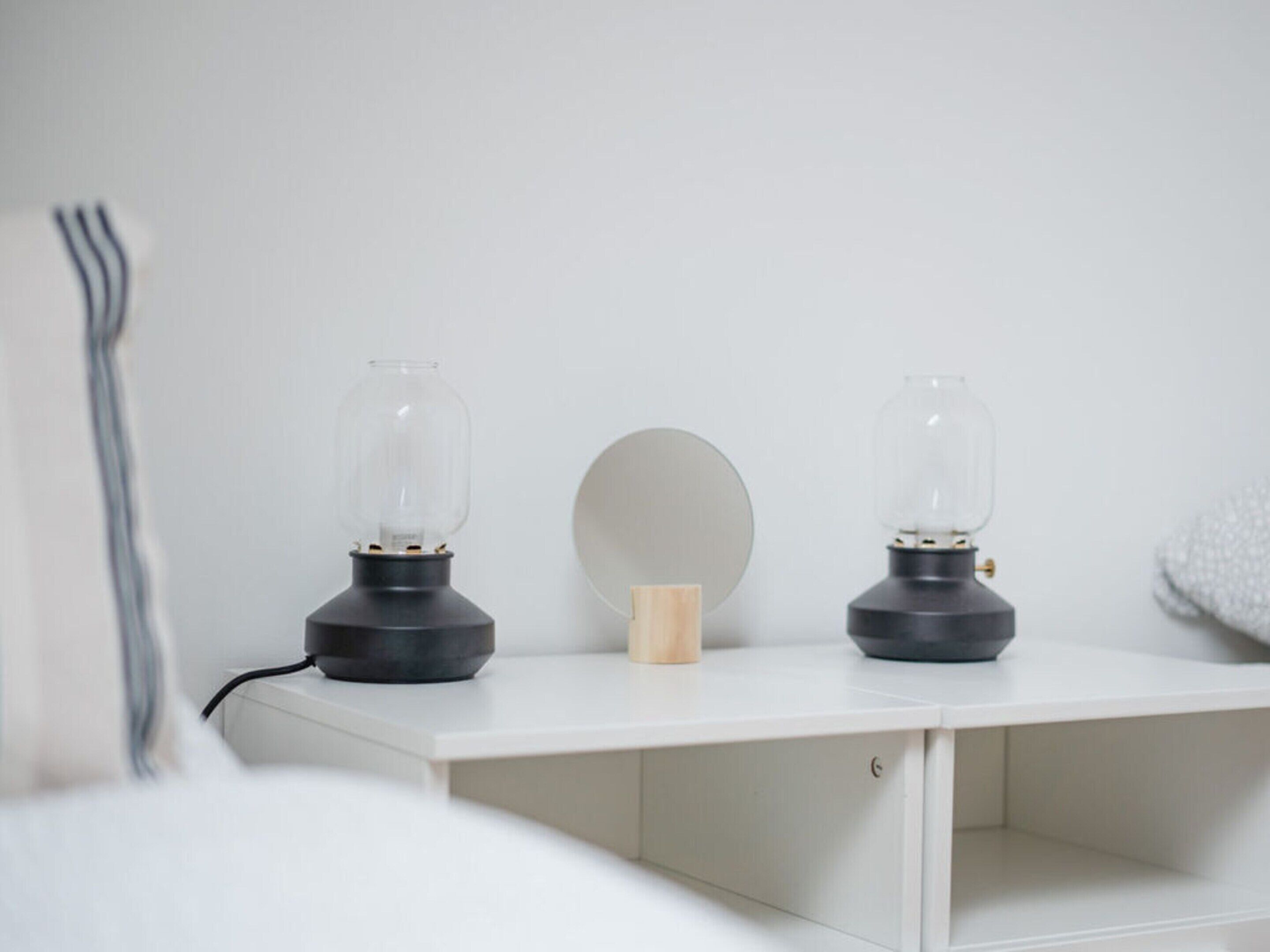 A white bedside table with two glass lamps and a wooden block.