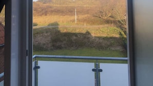 Blick aus einem Fenster mit Metallgeländer auf eine ländliche Landschaft mit Hügeln und spärlicher Vegetation.