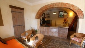 Un interior acogedor con mobiliario de mimbre, piso de piedra y una zona de cocina bajo un arco de ladrillo.