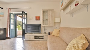 Un soggiorno con televisore su un supporto in legno, un divano beige con cuscini decorati, una lampada e un quadro appeso al muro.