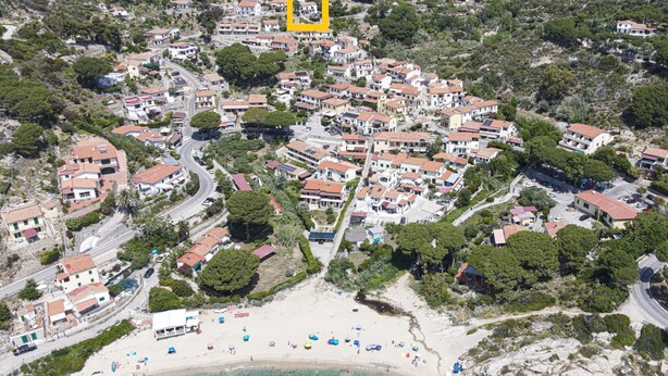 Vista aerea di una cittadina costiera con edifici residenziali, una spiaggia e acque turchesi cristalline.