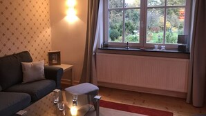 A living room with a sofa, a glass coffee table, a radiator, and a window with curtains. - Hansel und Gretel (Kassel)