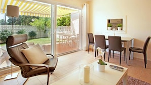 A modern living room with a sofa, dining table, chairs, and a glass door leading to an outdoor area with a yellow-striped awning. - Belvilla by OYO Villa Costabellas (Marbella)
