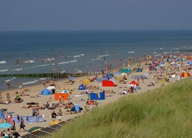 Una playa concurrida con numerosas tiendas de campaña y sombrillas, una orilla arenosa y el océano al fondo.
