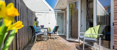 A patio with a table and chairs, a wooden fence, and a sliding glass door leading to a covered area.