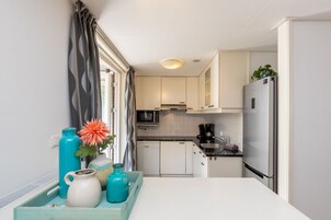 Una cocina compacta con armarios blancos, microondas, cafetera y refrigerador.