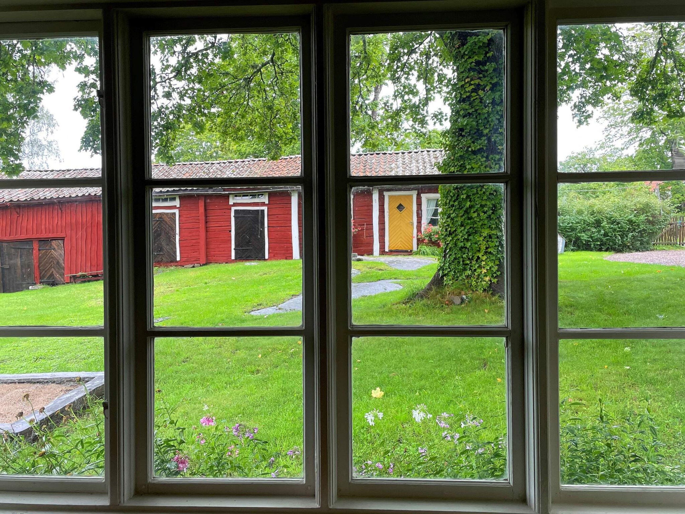 A view through a window with a red barn, a yellow door, and a green lawn.