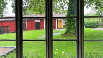 A view through a window with a red barn, a yellow door, and a green lawn.