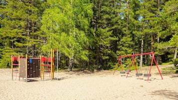 A playground with swings and climbing structures, surrounded by trees.