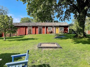 A red wooden building with a tiled roof, surrounded by a grassy lawn and trees. - 4 Person Holiday Home in Bjorko (Björkö)
