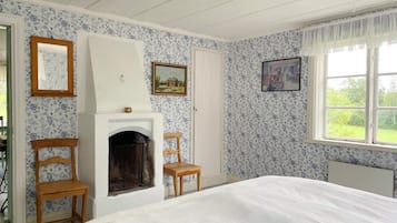 A bedroom with a fireplace, two wooden chairs, a bed, and floral wallpaper.
