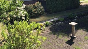 A single-story house with a front porch, a small attached garage, and a well-maintained garden with various plants and a wooden bench. - Bungalow Oberspreewald 4 (Schwielochsee)