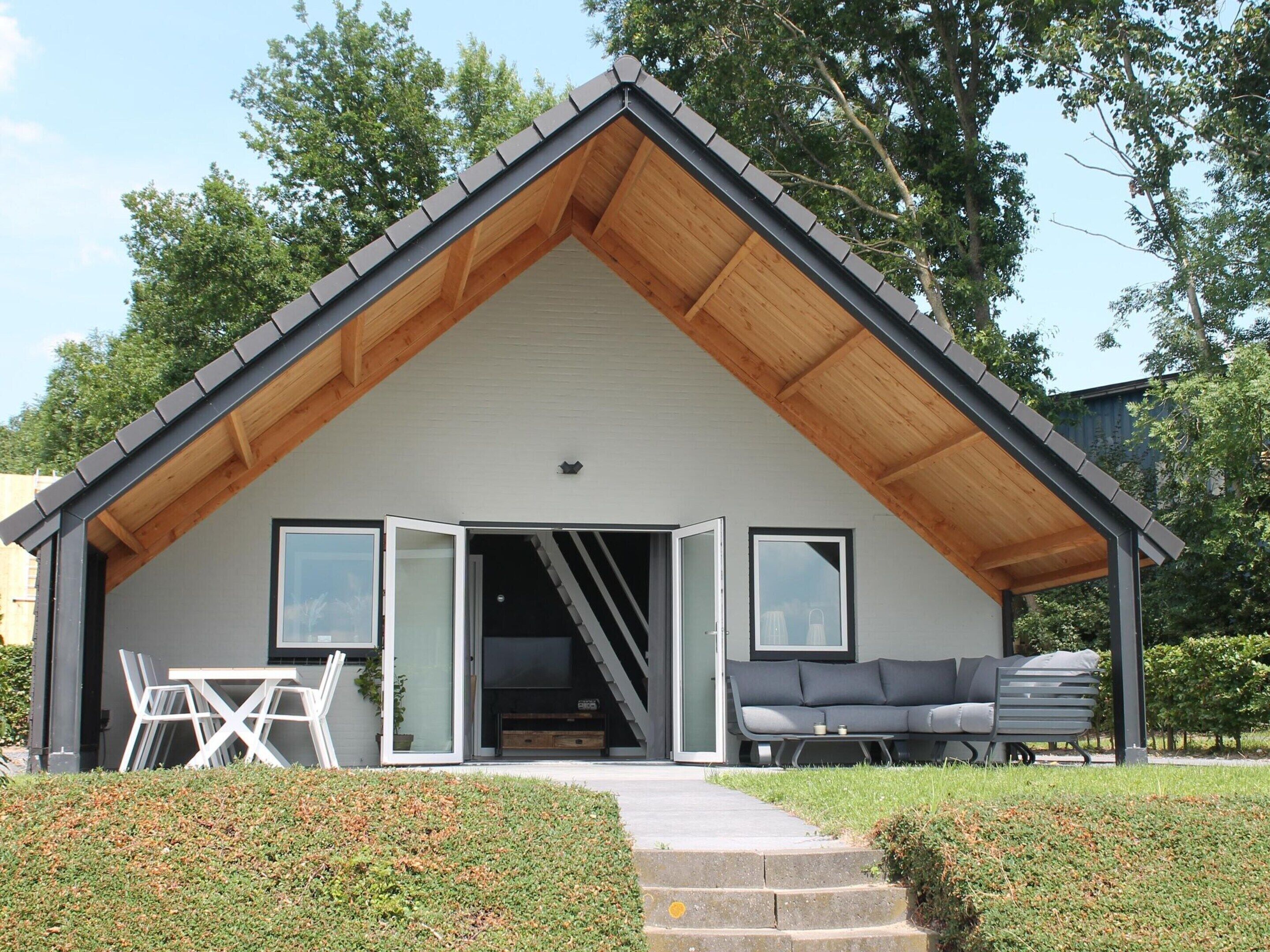 Een modern huis met een houten puntgevel, een glazen deuropening, een terras met tuinmeubilair en een verzorgd gazon.
