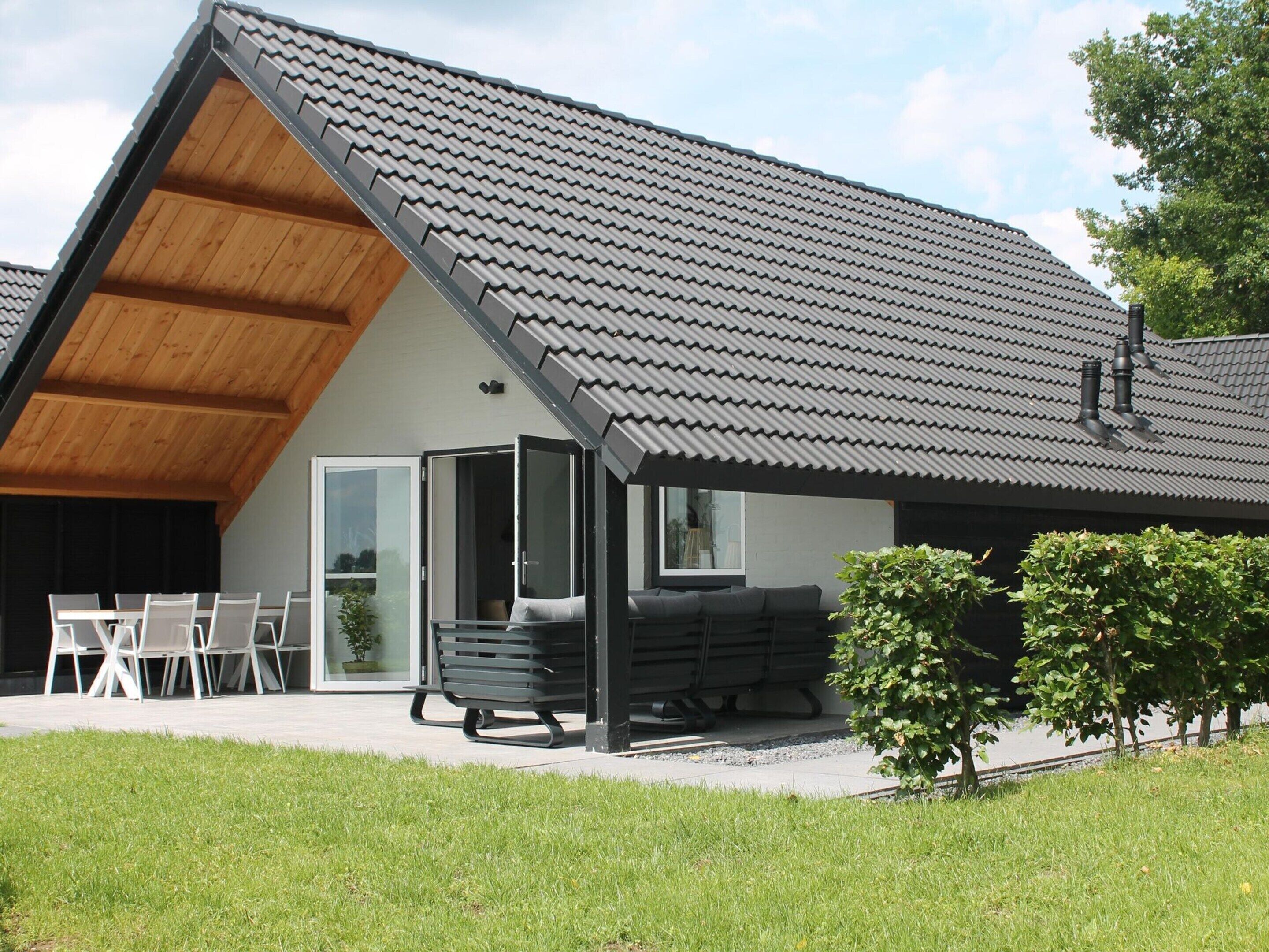 Une maison moderne avec un toit en pente, un patio couvert avec des meubles d’extérieur et un petit jardin.