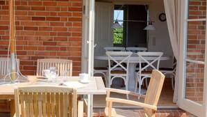 An open patio with a table and chairs, a brick wall, and a door leading to an interior room. - Hogelia Comfortable Holiday Residence (Steinbergkirche)