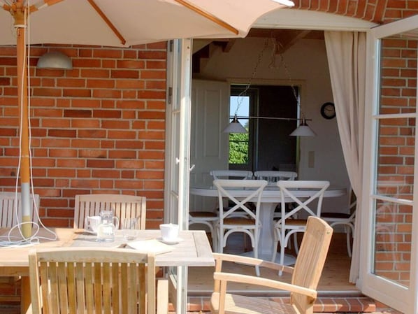 An open patio with a table and chairs, a brick wall, and a door leading to an interior room.