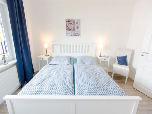Une chambre avec un lit simple, deux tables de chevet, une chaise et un élément décoratif mural.