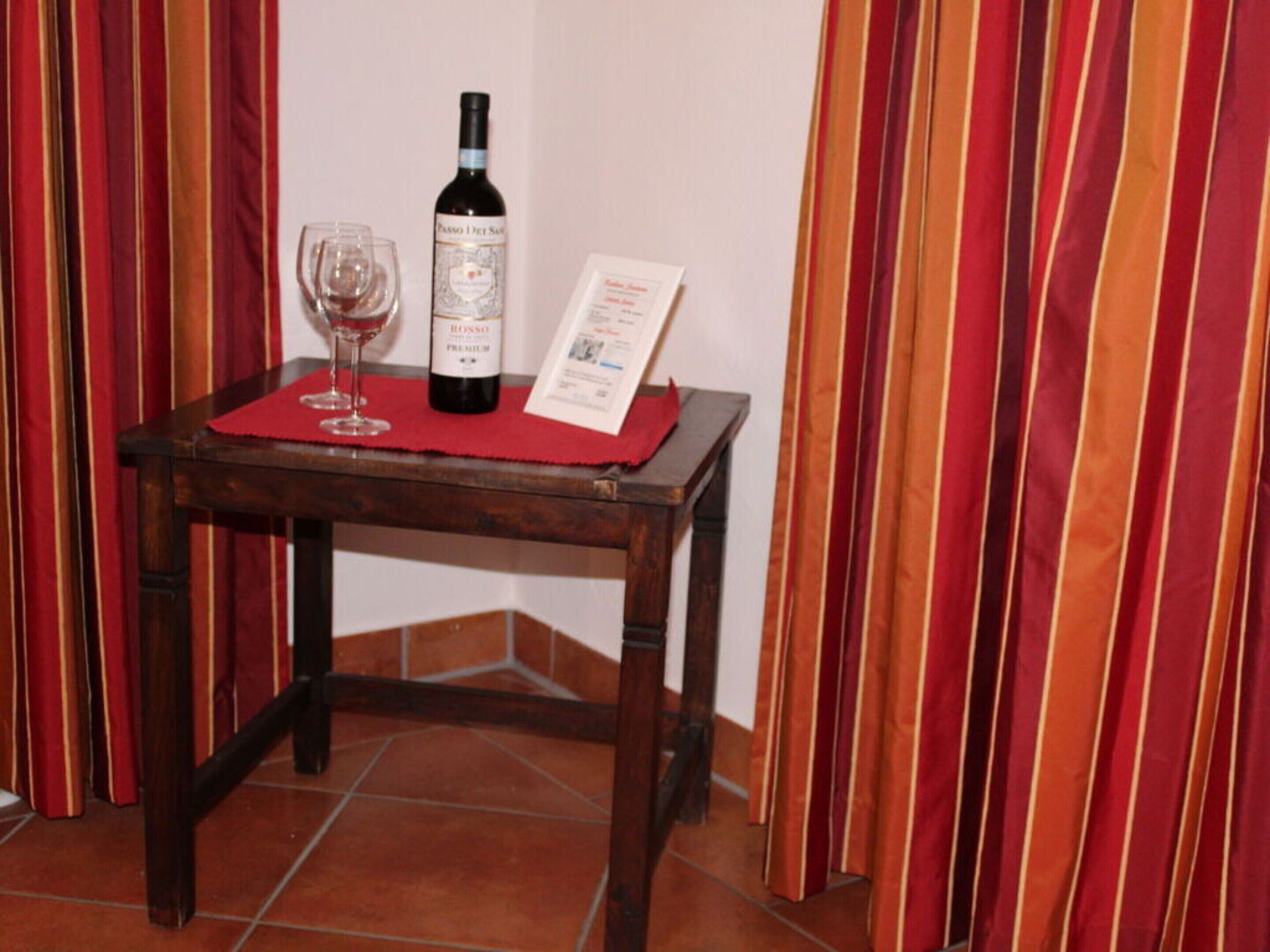 Een houten tafel met een rode tafelmat, een wijnfles en een glas rode wijn.