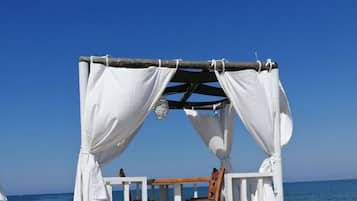 En strandhytte med træterrasse og hvide gardiner, med udsigt over havet.
