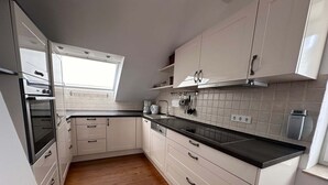 A modern kitchen with white cabinets, a black countertop, and a wooden floor. - Shared Holiday in two Separate Flats (Brilon)