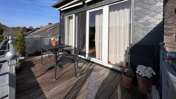 A modern balcony with a wooden deck, a table with chairs, and potted plants. - Shared Holiday in two Separate Flats (Brilon)
