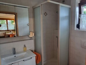 A bathroom with a shower, a sink with a soap dispenser, a mirror, and a window with a curtain. - House Schwarzwaldblick Ettenheim (Ettenheim)