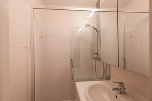 Bathroom features a glass-enclosed shower, handheld showerhead, and wall-mounted faucet.
