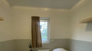 A small, single-room hotel room with a window, a radiator, and a nightstand. - Pavilion 4 People (Zorgvlied)