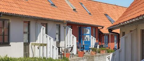 A row of traditional houses with red-tiled roofs and white walls, featuring a central building with a blue door and a staircase leading to a covered porch.