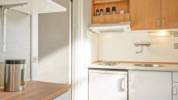 Cocina compacta con armarios blancos, hervidor de acero inoxidable, lavabo y estufa.