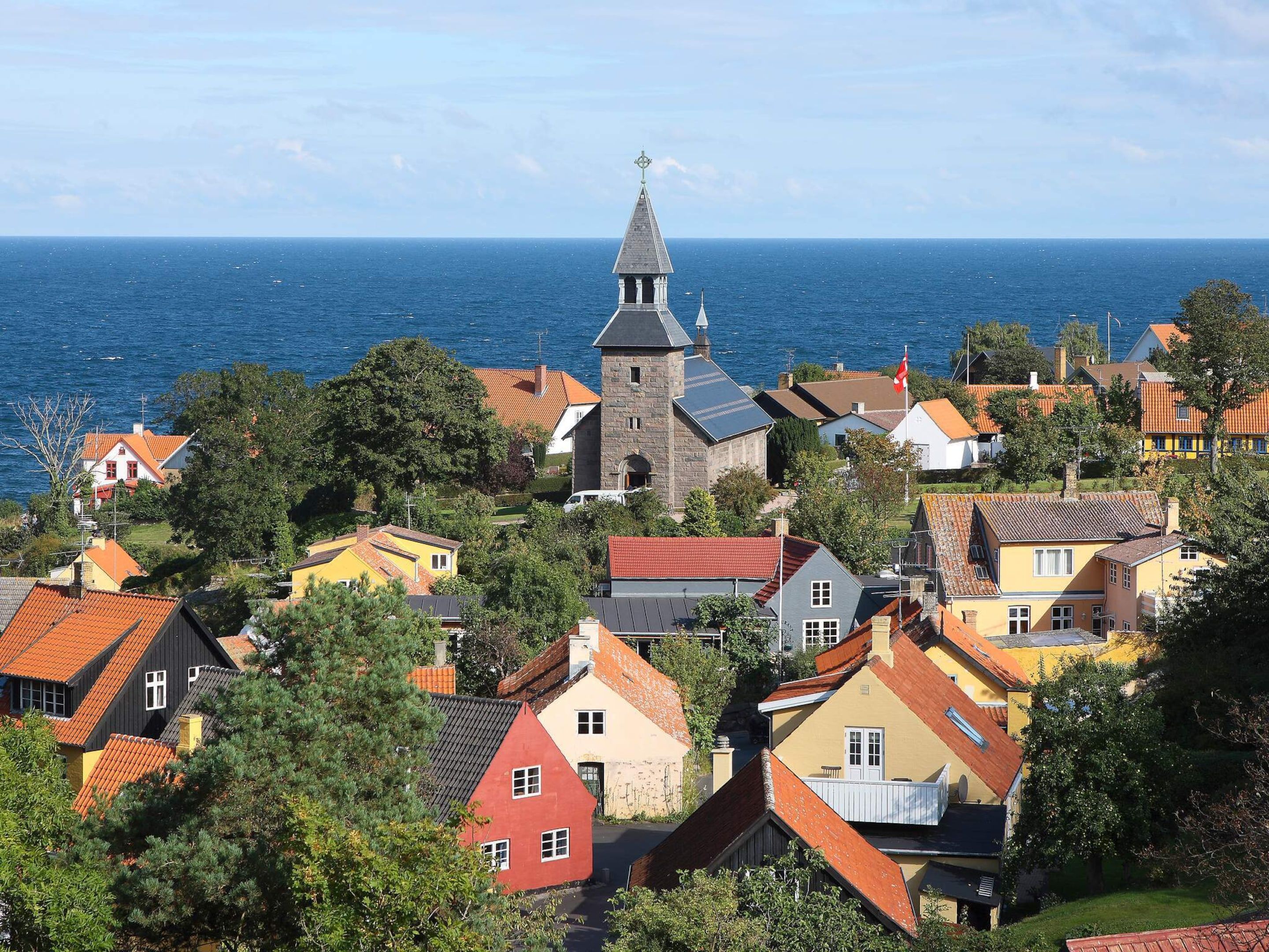 Un village côtier aux maisons aux couleurs vives, une église imposante surmontée d’un clocher et une vue sur la mer.