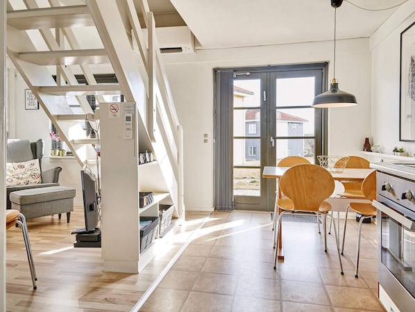 A modern kitchen with a dining area, wooden chairs, and a staircase leading to a loft. - 4 Person Holiday Park Home in Gudhjem (Gudhjem)