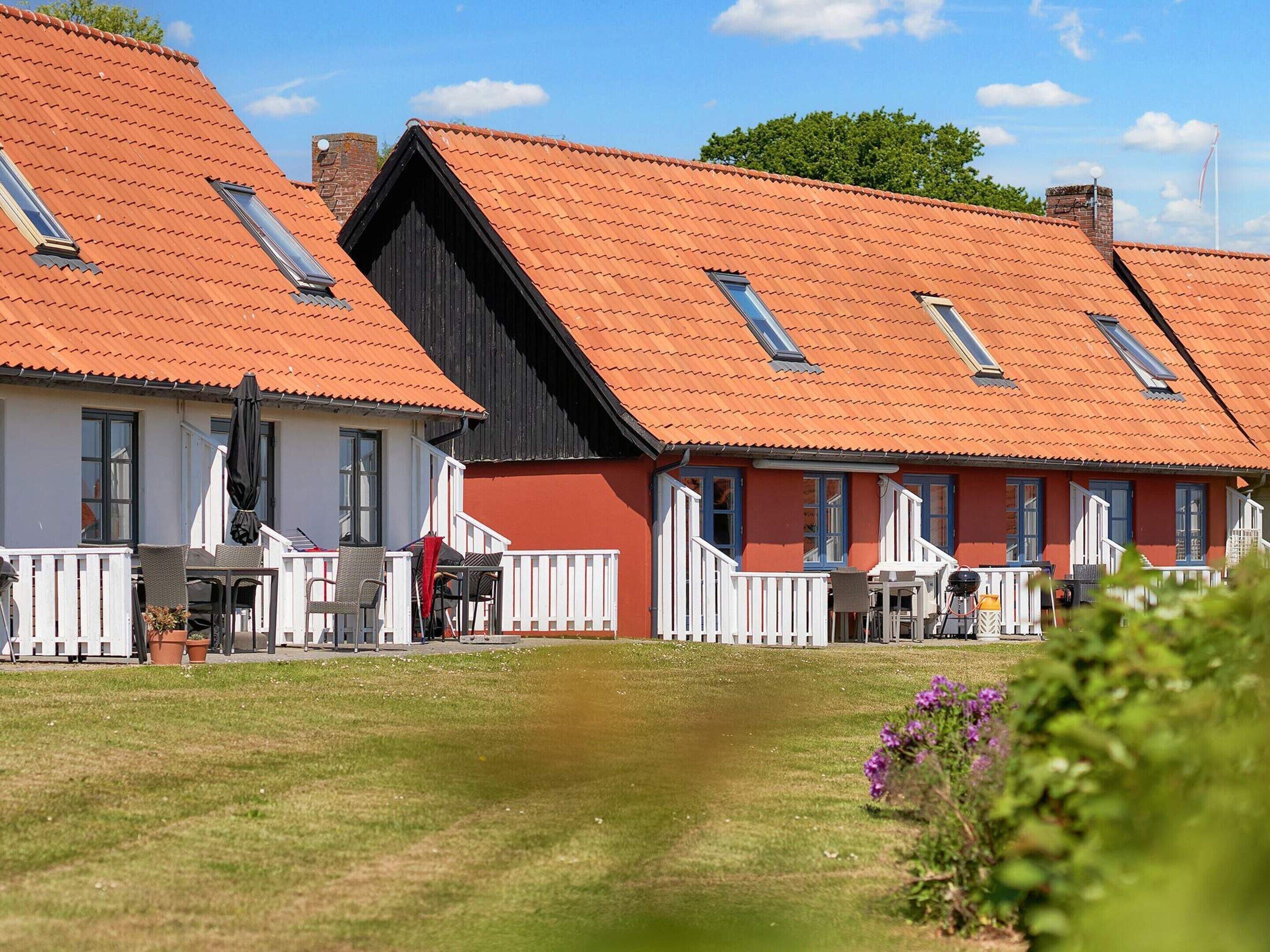 A row of traditional red-roofed cottages with white railings, a grassy lawn, and a clear sky.