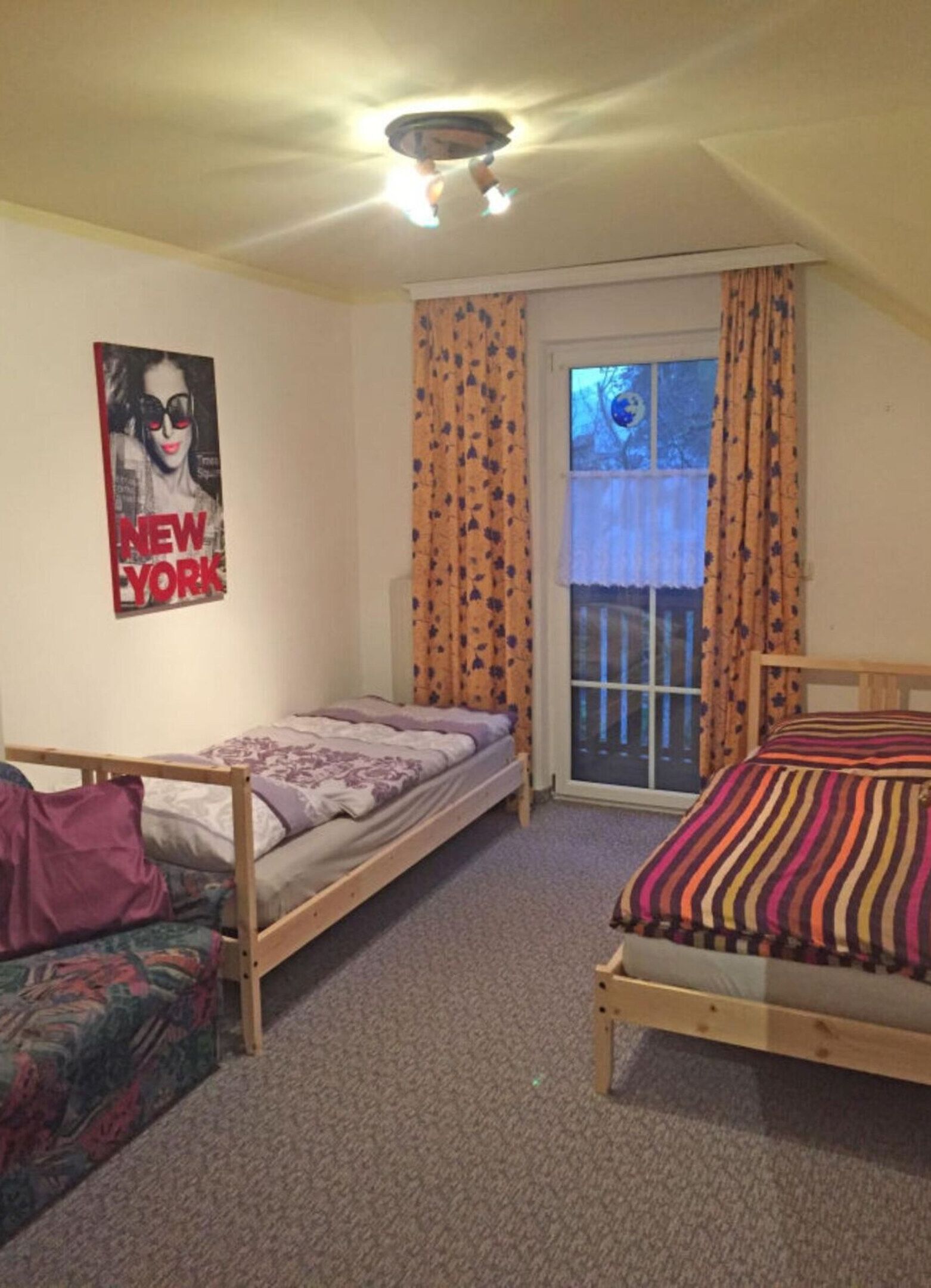 A small, cozy room with two single beds, a poster on the wall, and a window with curtains.