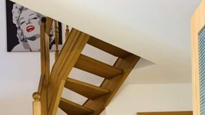 Una escalera de madera con barandilla, un radiador y una puerta con un símbolo negro.
