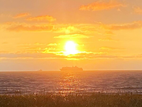 A sunset over a body of water with a ship in the distance.