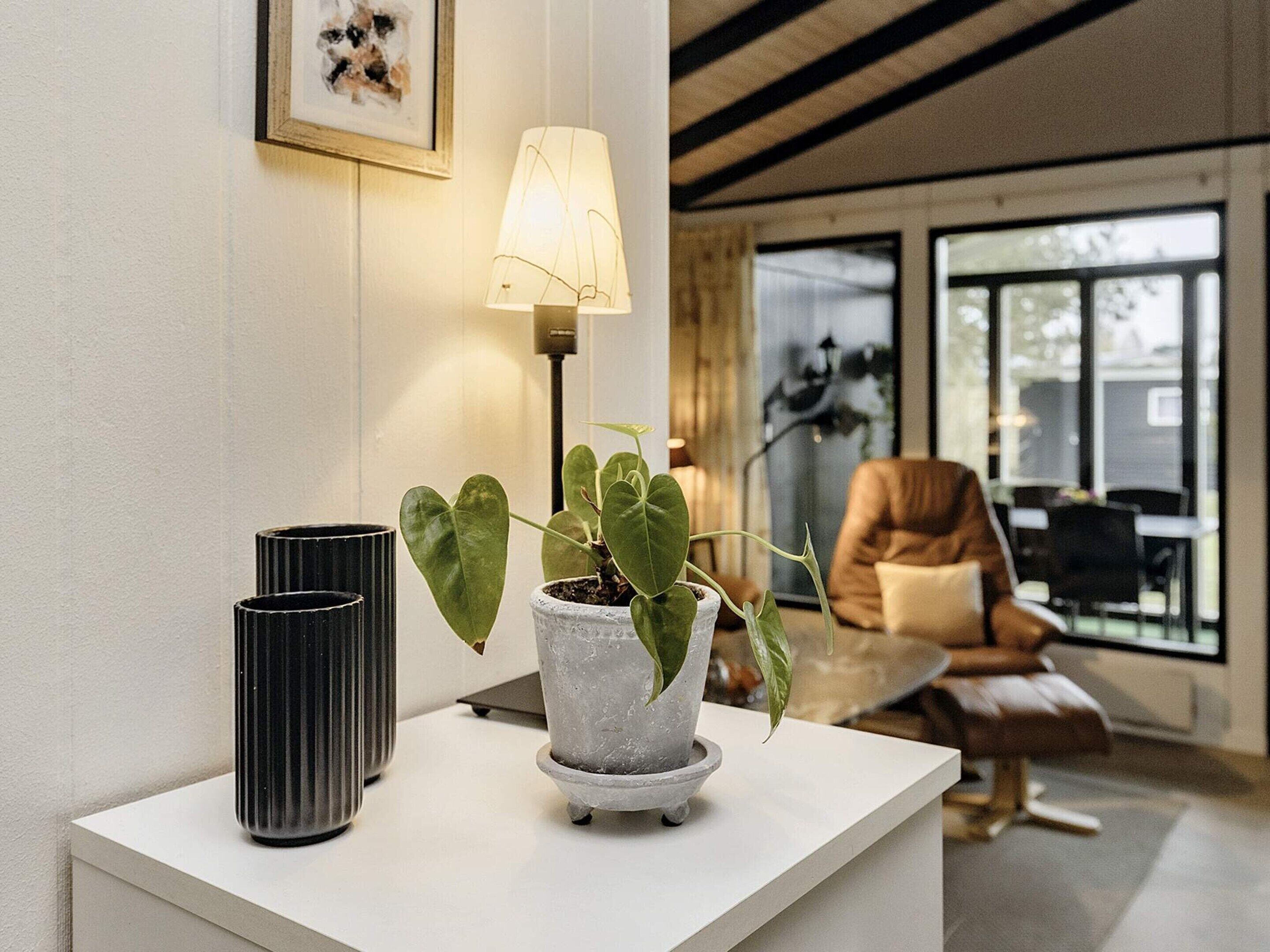 Ein modernes Wohnzimmer mit einem weißen Konsolentisch, einer Topfpflanze, einer Lampe und einem Ledersessel.