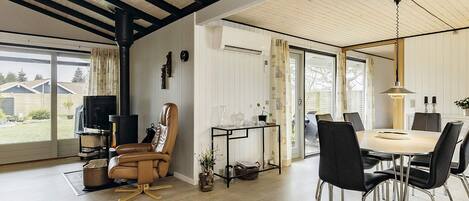 A modern living room with a fireplace, a dining area with a table and chairs, and a large window offering a view of the outdoors.
