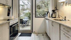 A compact kitchen with a built-in oven, a sink, and a window overlooking a garden. - 4 Star Holiday Home in Vaeggerlose (Vaeggerlose)