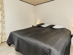 Un lit bien fait, recouvert d’une courtepointe sombre à motifs et agrémenté d’oreillers, une lampe de chevet et un rideau à motifs géométriques.