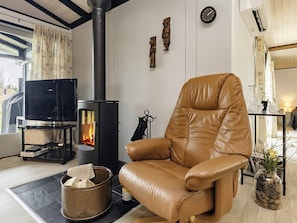 Une pièce avec un fauteuil en cuir, une cheminée, un téléviseur et une fenêtre avec des rideaux.