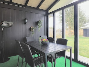 Une pièce avec une table en bois foncé, des chaises en osier, une moquette verte et une vue sur une cour par de grandes fenêtres.