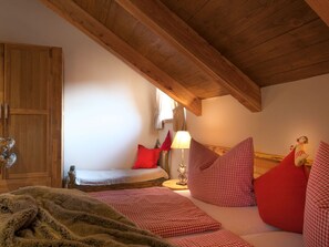 A cozy bedroom with a wooden ceiling, a bed with red pillows, a lamp, and a small statue on the nightstand.