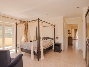 Un espacioso dormitorio con cama con dosel, una zona de estar con una silla y vistas al exterior a través de grandes puertas correderas.