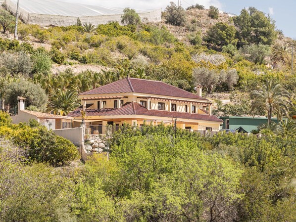 A two-story house with a tiled roof, surrounded by dense vegetation and hills. - Belvilla by OYO Villa Nancy (Callosa d' En Sarria)