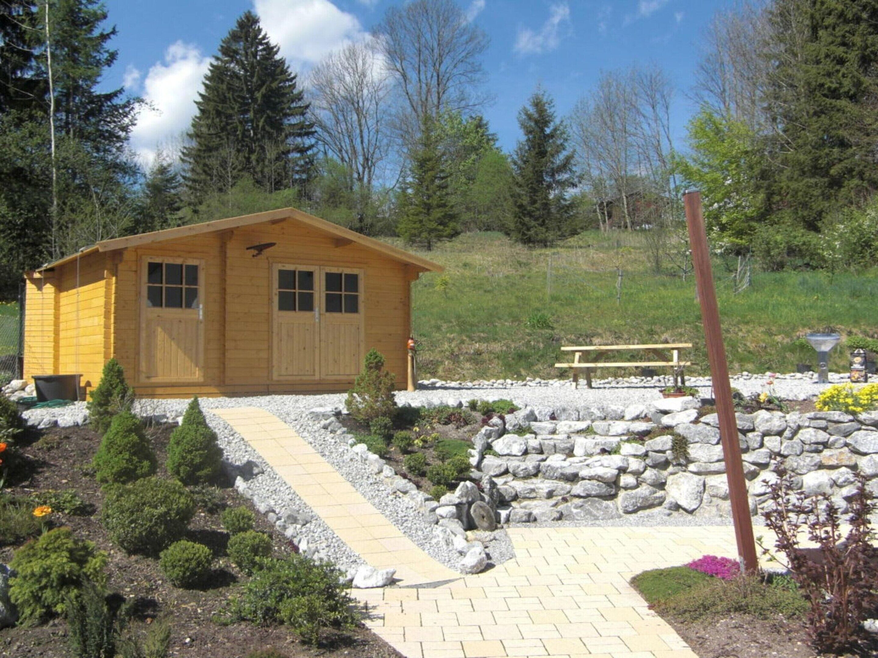 A wooden cabin with a stone pathway leading to it, surrounded by greenery and a picnic table.