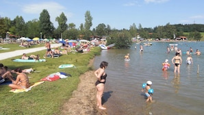 A lakeside setting with people relaxing on the grass and in the water. - Holiday Apartment at the Rose Garden (Fuessen)